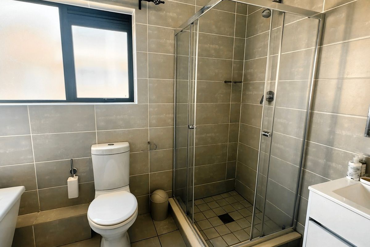 A functional bathroom featuring a glass-enclosed shower, modern vanity with basin, toilet, and neutral floor-to-ceiling tiling.