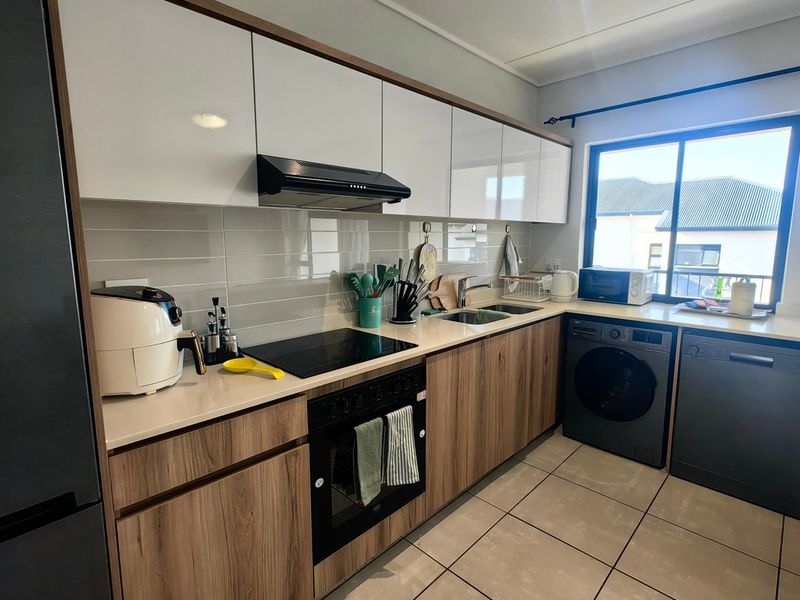 Modern kitchen featuring wood-grain and white cabinetry, stone countertops, integrated appliances, and tiled flooring with a bright window view.