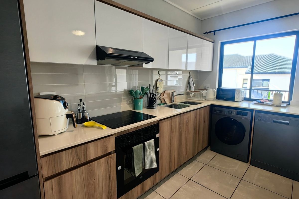Modern kitchen featuring wood-grain and white cabinetry, stone countertops, integrated appliances, and tiled flooring with a bright window view.