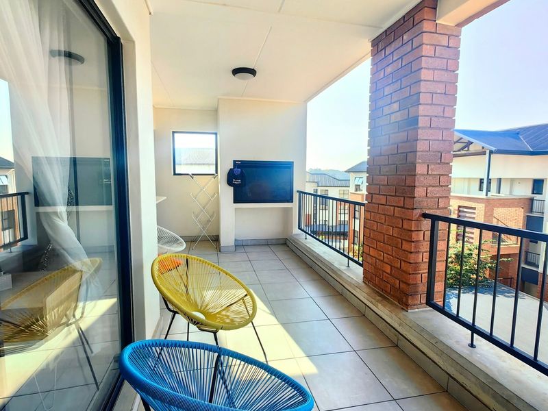 A covered balcony featuring tiled flooring, a built-in braai, and a metal balustrade, offering an outdoor space for relaxation.