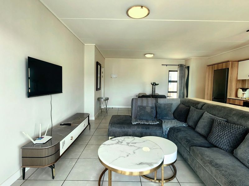 An open-plan living and kitchen area featuring neutral tiled flooring, modern flush mount lighting, and contemporary kitchen cabinetry in a well-maintained townhouse setting.
