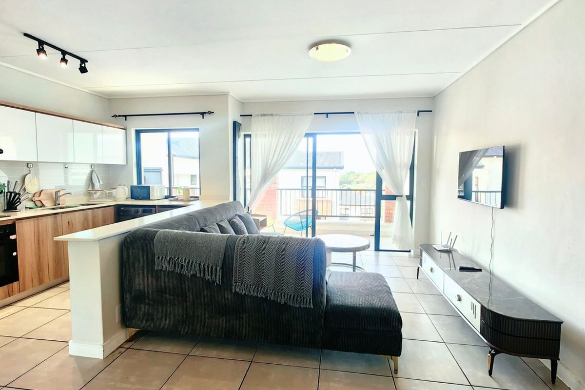 Modern open-plan living area featuring a contemporary kitchen with built-in cabinetry, tiled flooring, and seamless access to a private balcony through sliding glass doors.