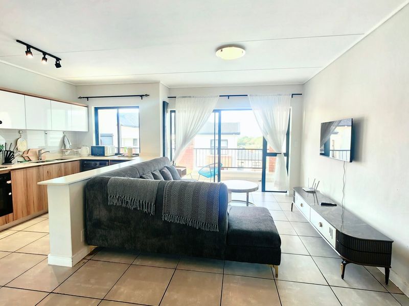 Modern open-plan living area featuring a contemporary kitchen with built-in cabinetry, tiled flooring, and seamless access to a private balcony through sliding glass doors.