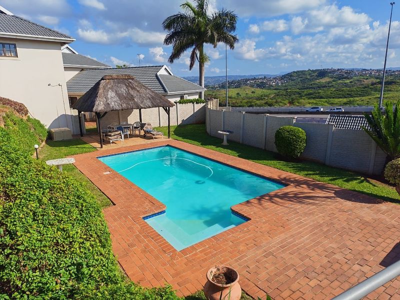 Outdoor pool area featuring a swimming pool, brick paved surround, and a thatched gazebo, set within a private garden with scenic views.
