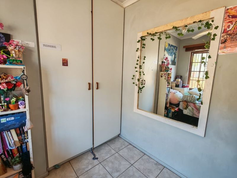 A bedroom featuring built-in cupboards, tiled flooring, and a window with security bars, offering a functional space with potential for cosmetic updates.