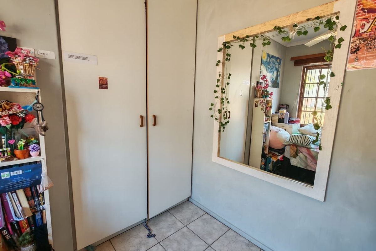 A bedroom featuring built-in cupboards, tiled flooring, and a window with security bars, offering a functional space with potential for cosmetic updates.