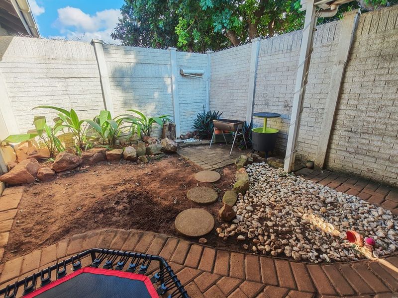A compact rear courtyard featuring a paved patio, stone landscaping, and a precast concrete boundary wall, offering potential for garden enhancement.