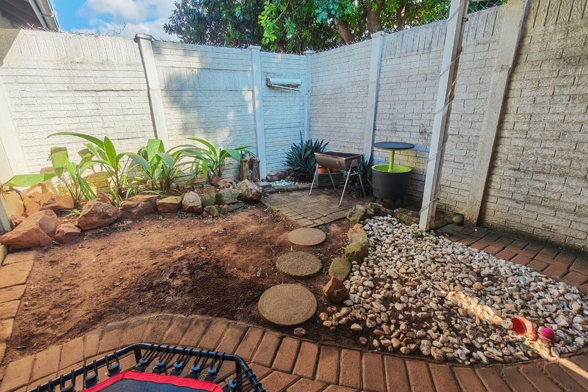 A compact rear courtyard featuring a paved patio, stone landscaping, and a precast concrete boundary wall, offering potential for garden enhancement.