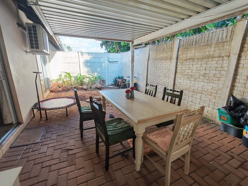 A covered outdoor patio area featuring brick paving, a corrugated metal roof, and a precast concrete boundary wall, suitable for outdoor dining.