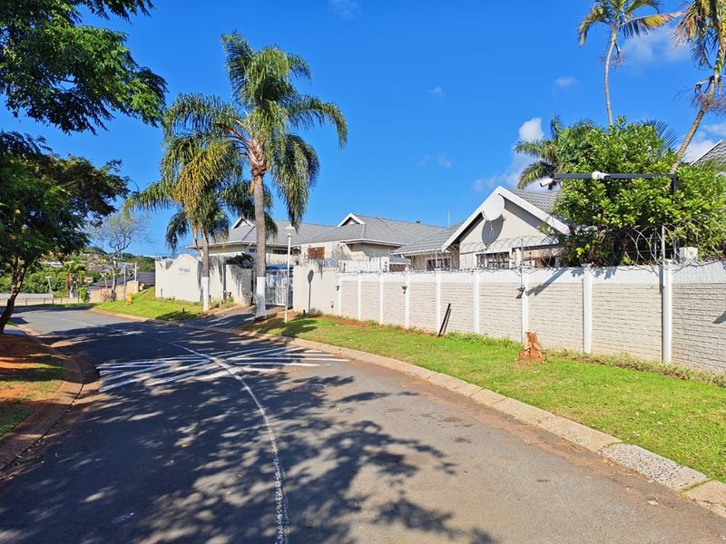 Street view of the townhouse complex featuring a perimeter wall with security fencing and mature palm trees.