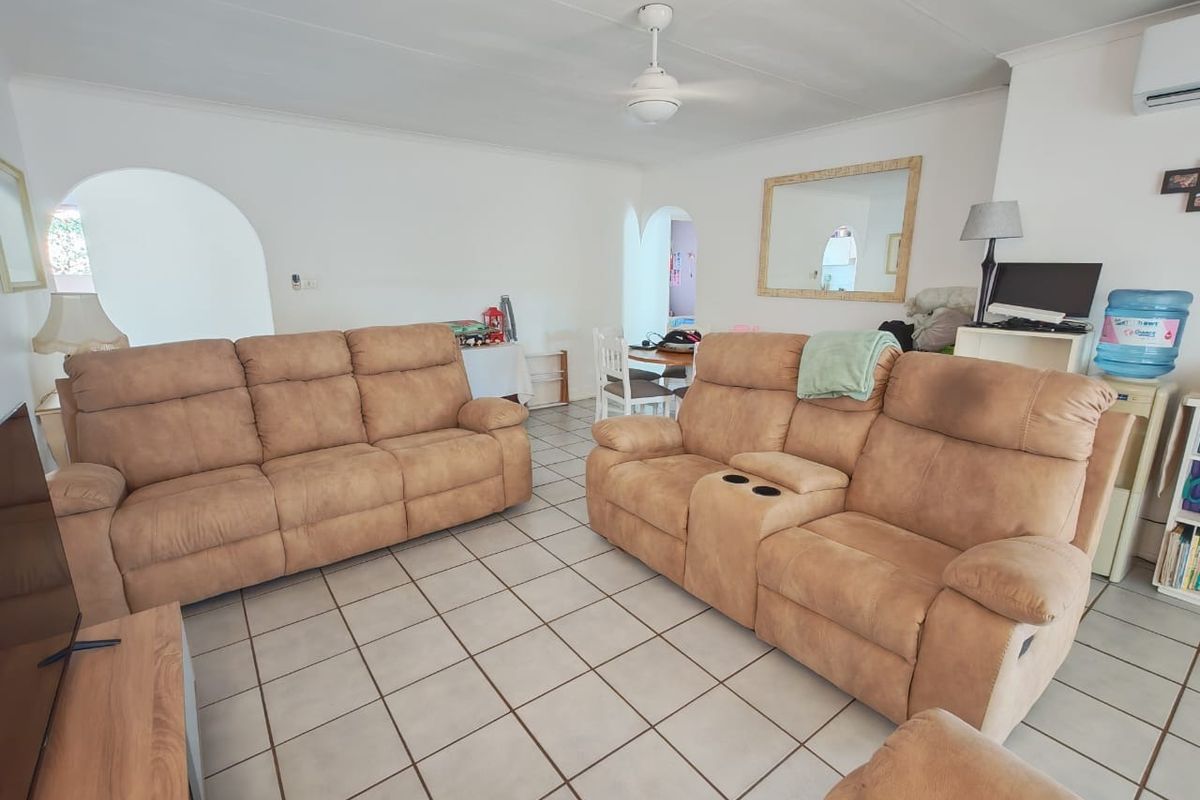 A spacious living room featuring ceramic tile flooring, a ceiling fan, and a split-system air conditioner, with arched doorways leading to adjacent areas.