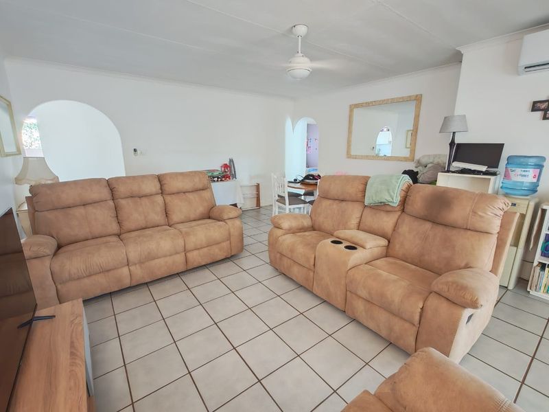 A spacious living room featuring ceramic tile flooring, a ceiling fan, and a split-system air conditioner, with arched doorways leading to adjacent areas.