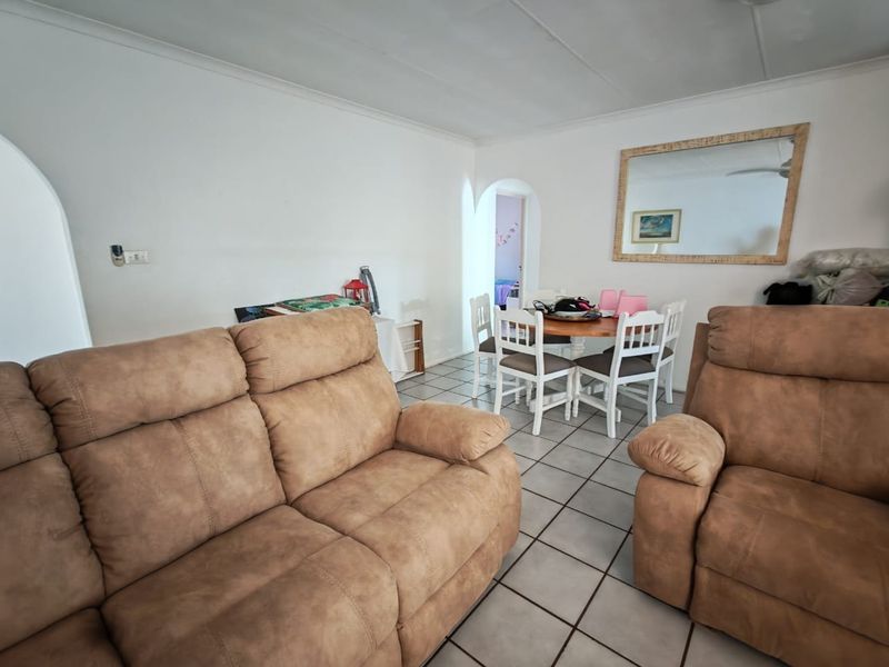A living and dining area featuring ceramic floor tiles, coved ceilings, and an arched doorway leading to adjacent rooms.