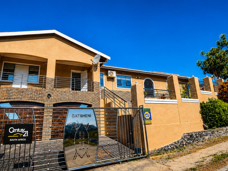 Front elevation of a multi-level house featuring a brick and rendered facade, metal security gate, and an upper-level balcony.
