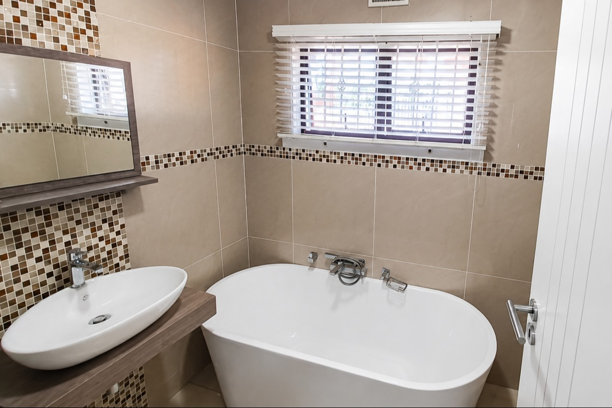 Modern bathroom featuring a freestanding bathtub, vessel sink with wall-mounted faucet, and decorative mosaic tile accents.