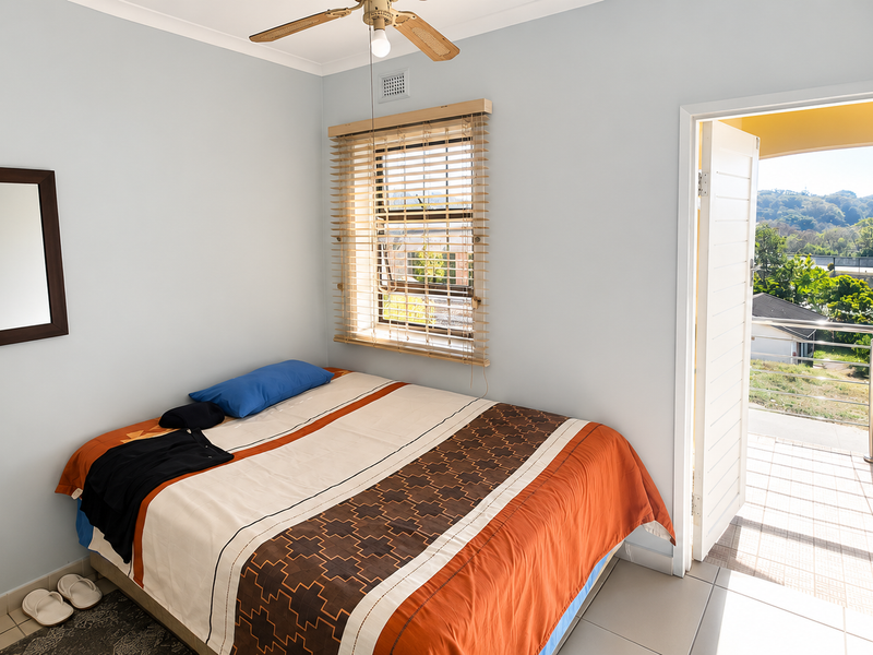 A bedroom featuring tiled flooring, a ceiling fan, and direct access to an outdoor balcony through a glass-panelled door.
