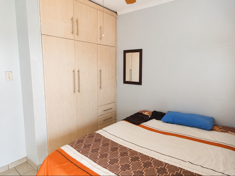 A functional bedroom featuring built-in wooden cupboards, neutral wall finishes, and window blinds, providing a practical and comfortable living space.