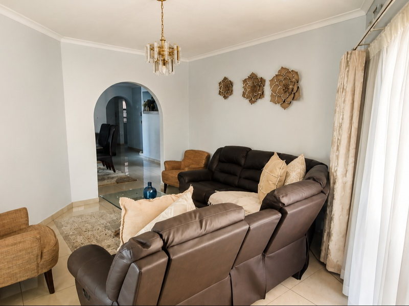 A bright and spacious living room featuring neutral tiled flooring, an elegant archway leading to adjacent areas, and a decorative chandelier.