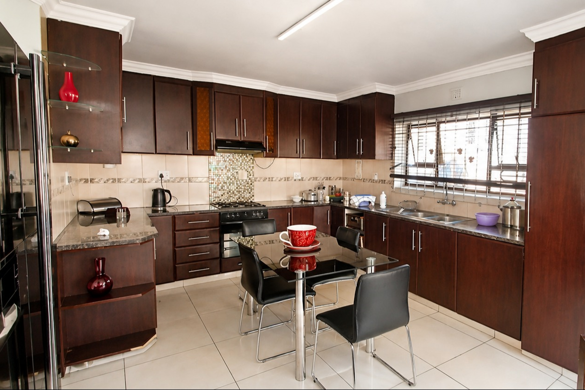 A functional kitchen featuring dark wood cabinetry, granite countertops, a mosaic tile backsplash, and integrated appliances with tiled flooring.
