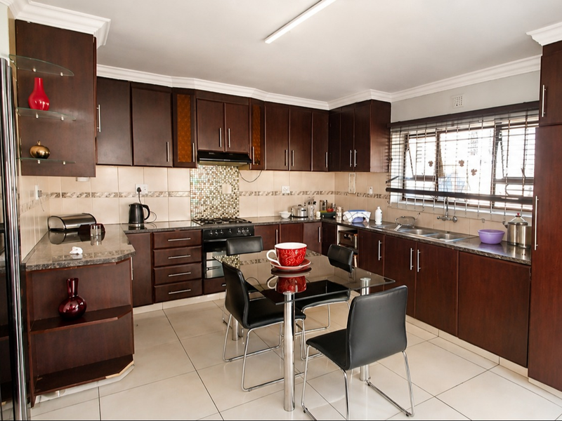 A functional kitchen featuring dark wood cabinetry, granite countertops, a mosaic tile backsplash, and integrated appliances with tiled flooring.