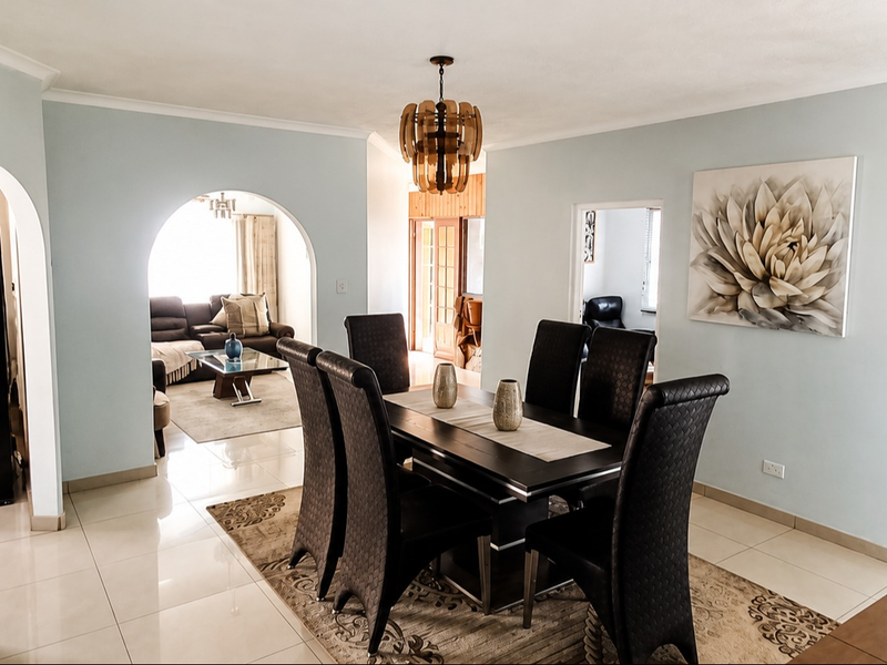 A bright dining room featuring tiled flooring, arched architectural transitions, and a central pendant light fixture, connecting to adjacent living spaces.