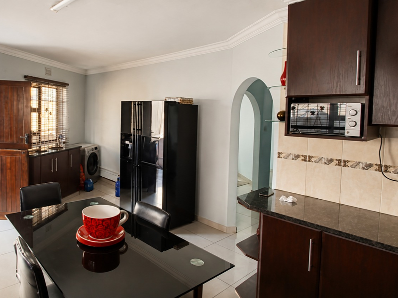 A functional kitchen featuring dark wood cabinetry, granite countertops, and tiled backsplash, with an adjacent dining area and direct access to the exterior.