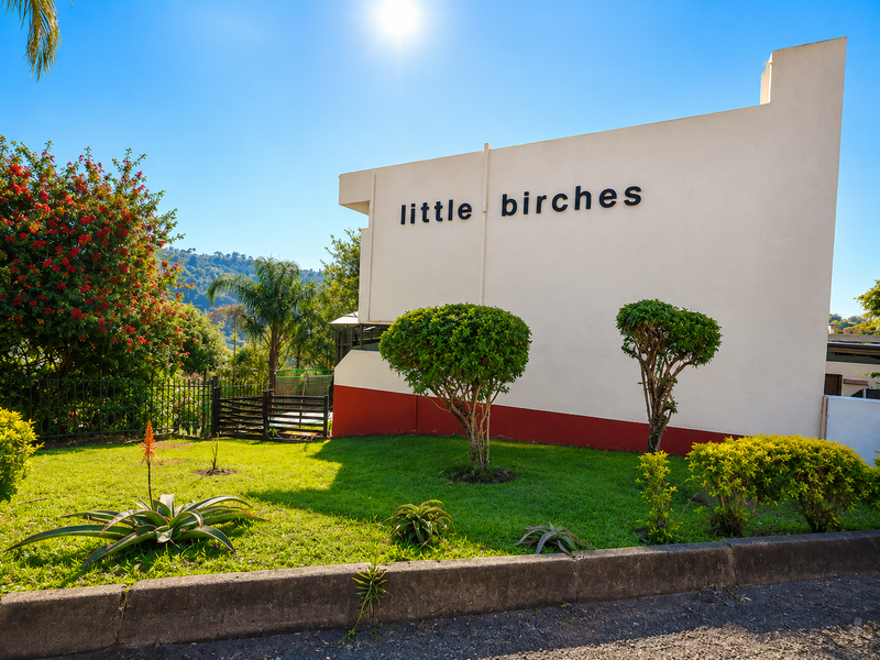 Front exterior view of the Little Birches apartment complex, featuring a well-maintained garden, perimeter fencing, and clear building signage.