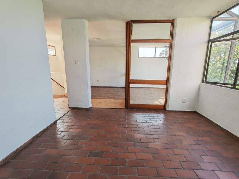 An empty living area featuring traditional terracotta tile flooring, a timber-framed glass door, and large windows providing natural light.