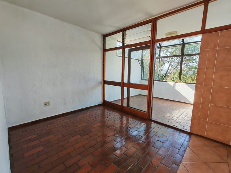 An empty living area featuring terracotta tile flooring and a large timber-framed glass partition leading to an enclosed balcony space.