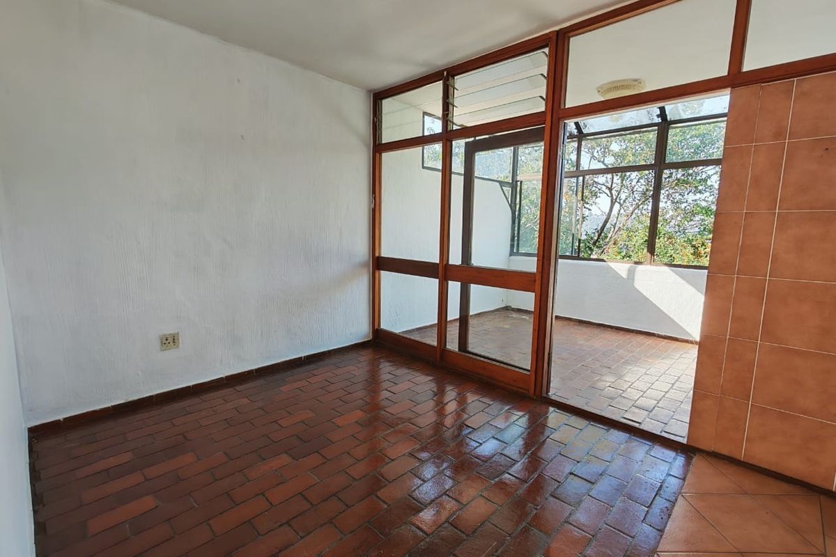 An empty living area featuring terracotta tile flooring and a large timber-framed glass partition leading to an enclosed balcony space.