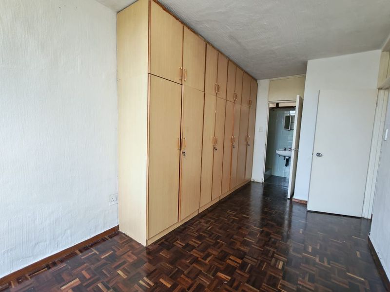 A vacant bedroom featuring extensive built-in wooden cupboards and traditional parquet flooring, with direct access to an adjacent bathroom.