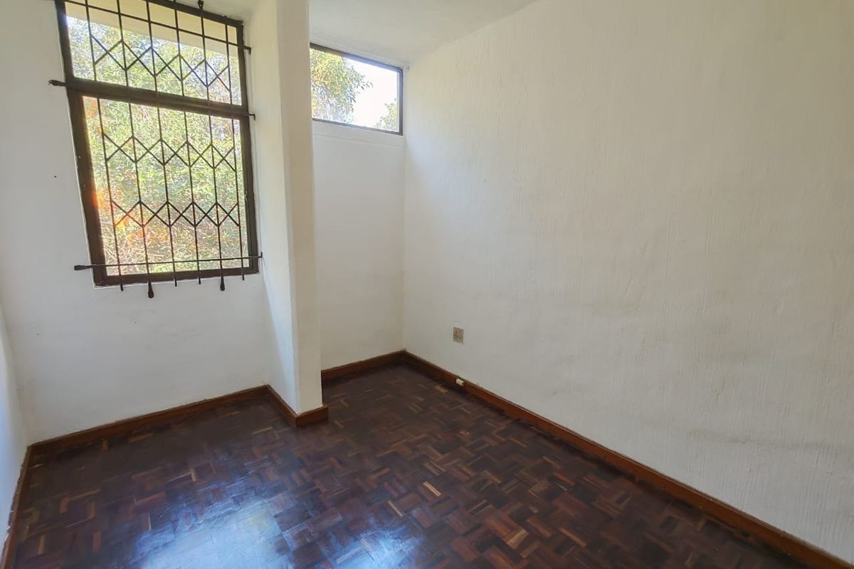 An empty bedroom featuring dark parquet flooring, white textured walls, and a window fitted with security bars.