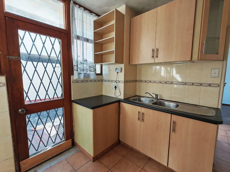 A functional kitchen featuring laminate cabinetry, tiled backsplash, and a stainless steel sink, with direct access to an outdoor area via a security door.