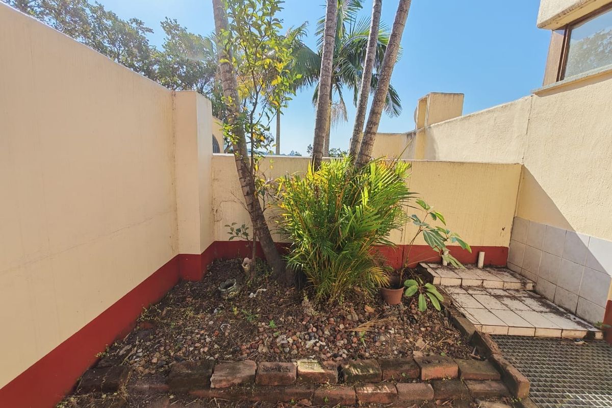 A small rear courtyard area featuring a garden bed, boundary walls, and tiled step access.