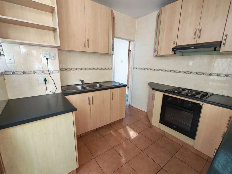 A functional kitchen featuring light wood-finish cabinetry, built-in oven and hob, double sink, and tiled surfaces throughout.