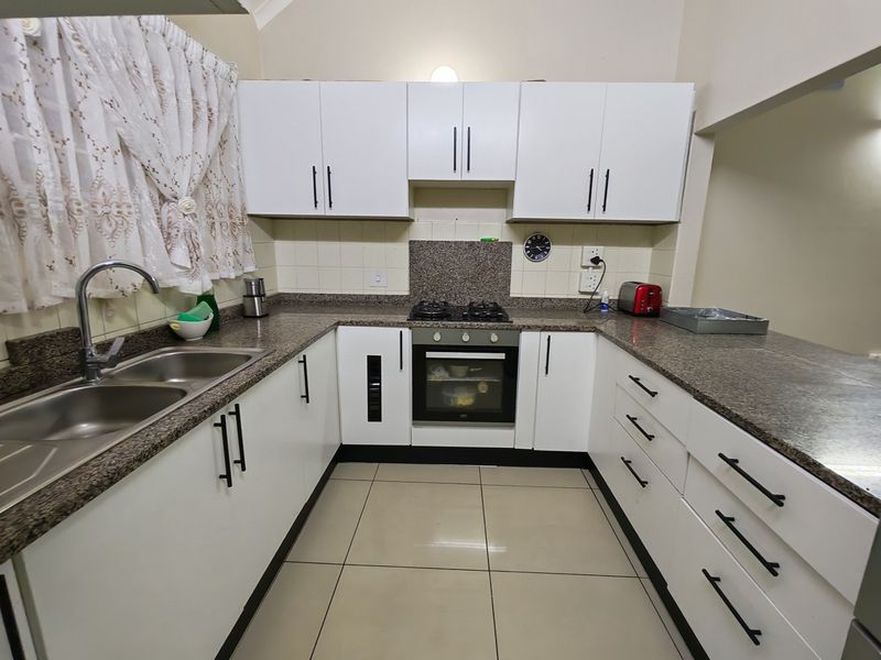A functional kitchen featuring white cabinetry, granite countertops, a gas hob, built-in oven, and a double bowl stainless steel sink.