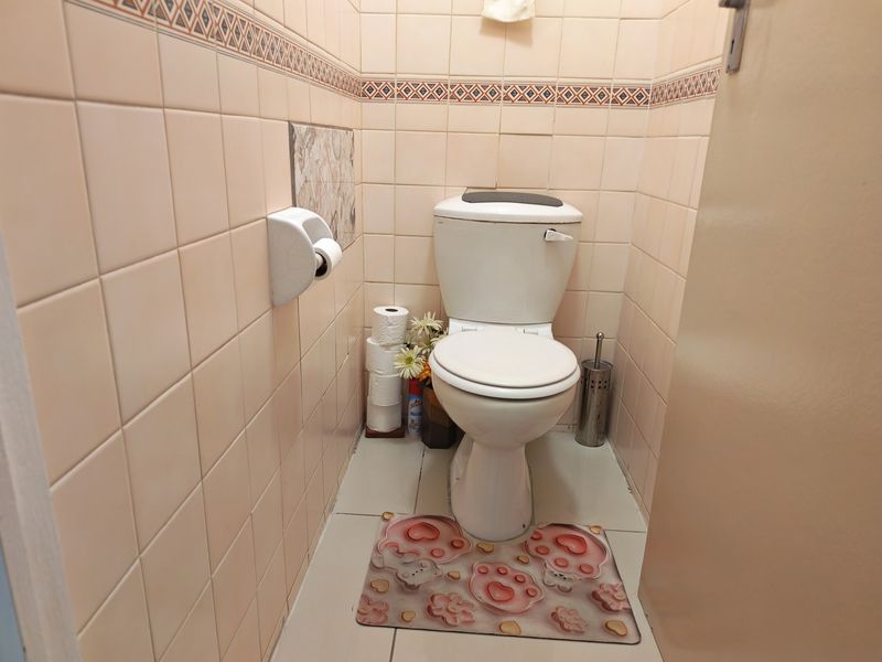 A compact guest bathroom featuring dated ceramic wall and floor tiles with a standard white toilet suite.