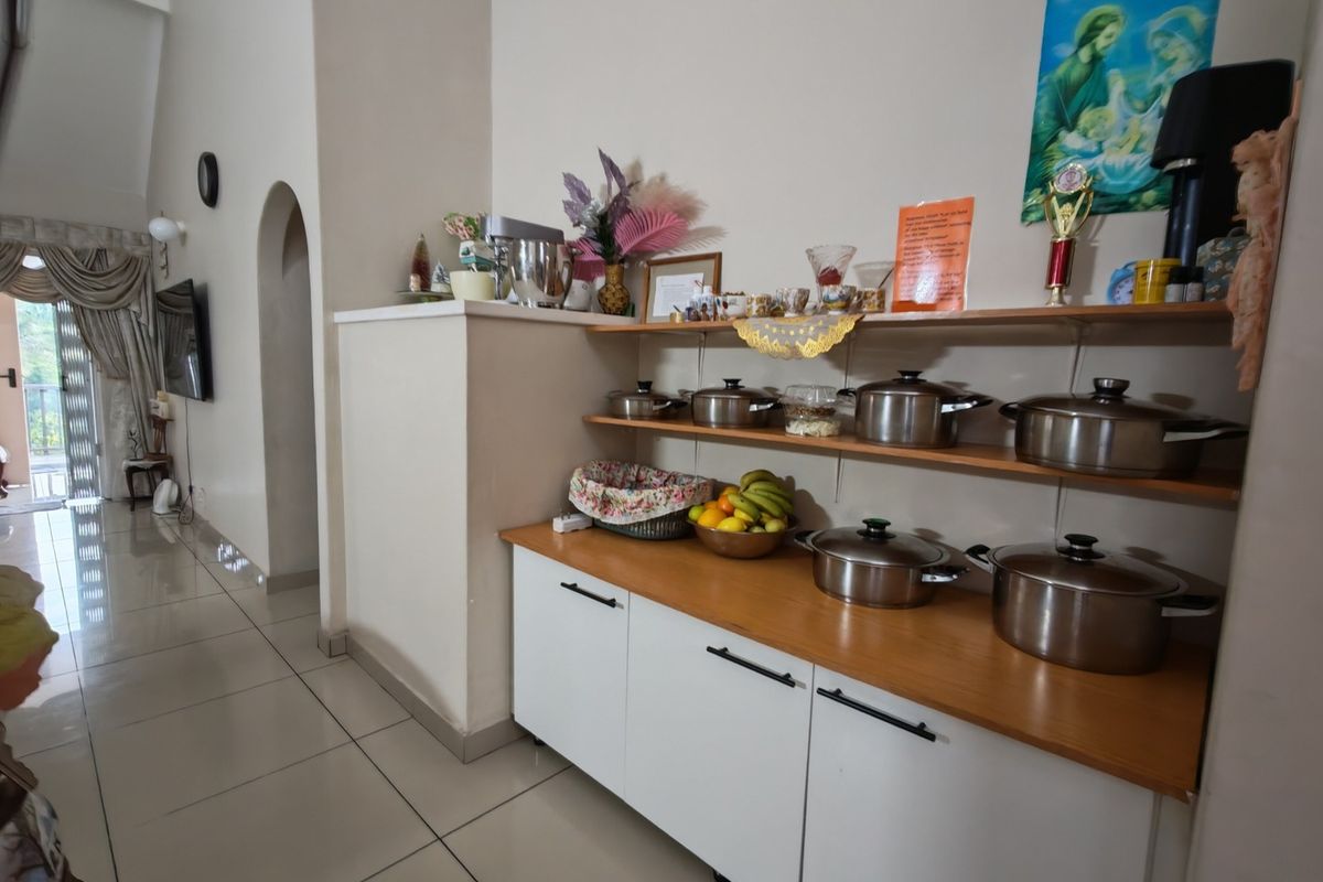A kitchen area featuring white base cabinetry with a wooden countertop, open shelving, and tiled flooring, leading into an adjacent living space.