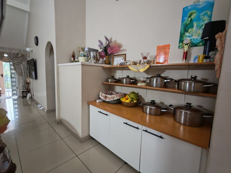 A kitchen area featuring white base cabinetry with a wooden countertop, open shelving, and tiled flooring, leading into an adjacent living space.