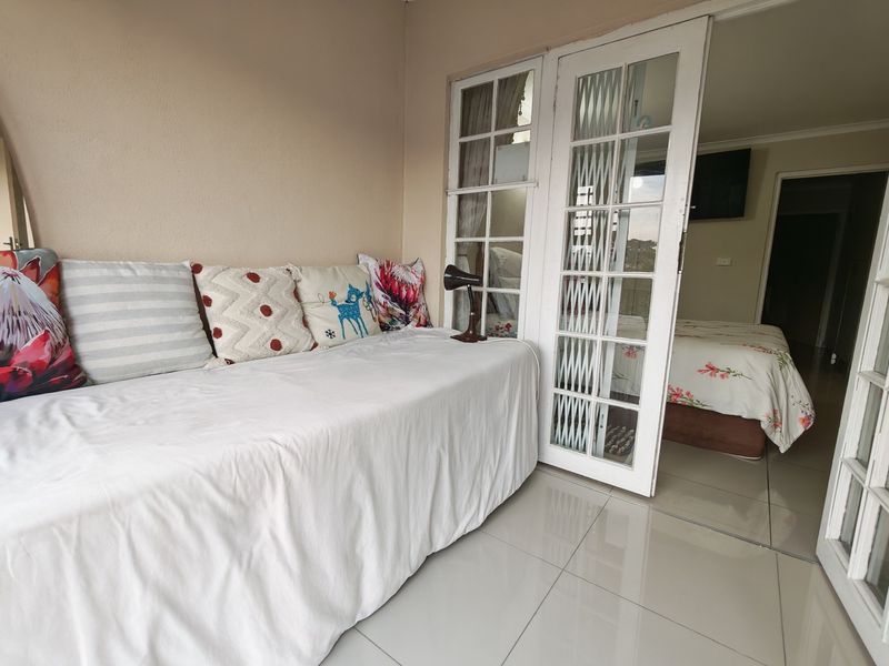 A covered patio area featuring tiled flooring and white french doors with integrated security gates, providing access to the interior bedroom space.