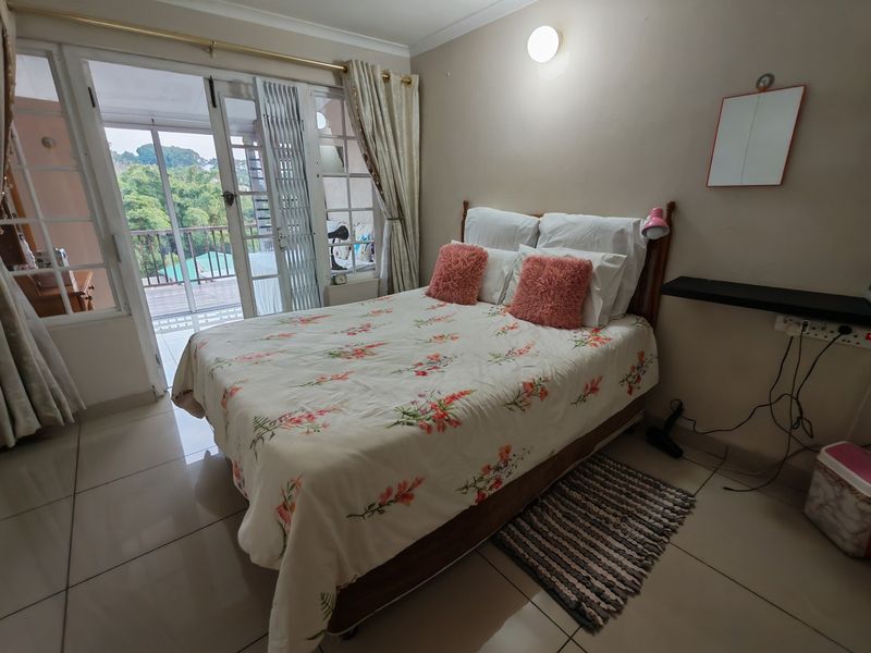 A bedroom featuring tiled flooring, a wall-mounted floating shelf, and a sliding glass door providing access to an outdoor balcony area.