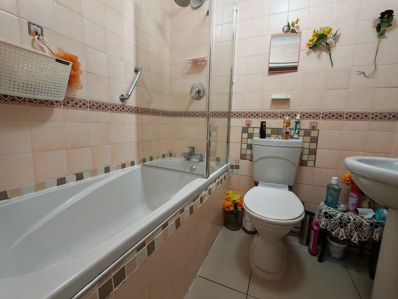 A functional bathroom featuring a bathtub with a glass shower screen, pedestal basin, and toilet, finished with dated wall tiling.