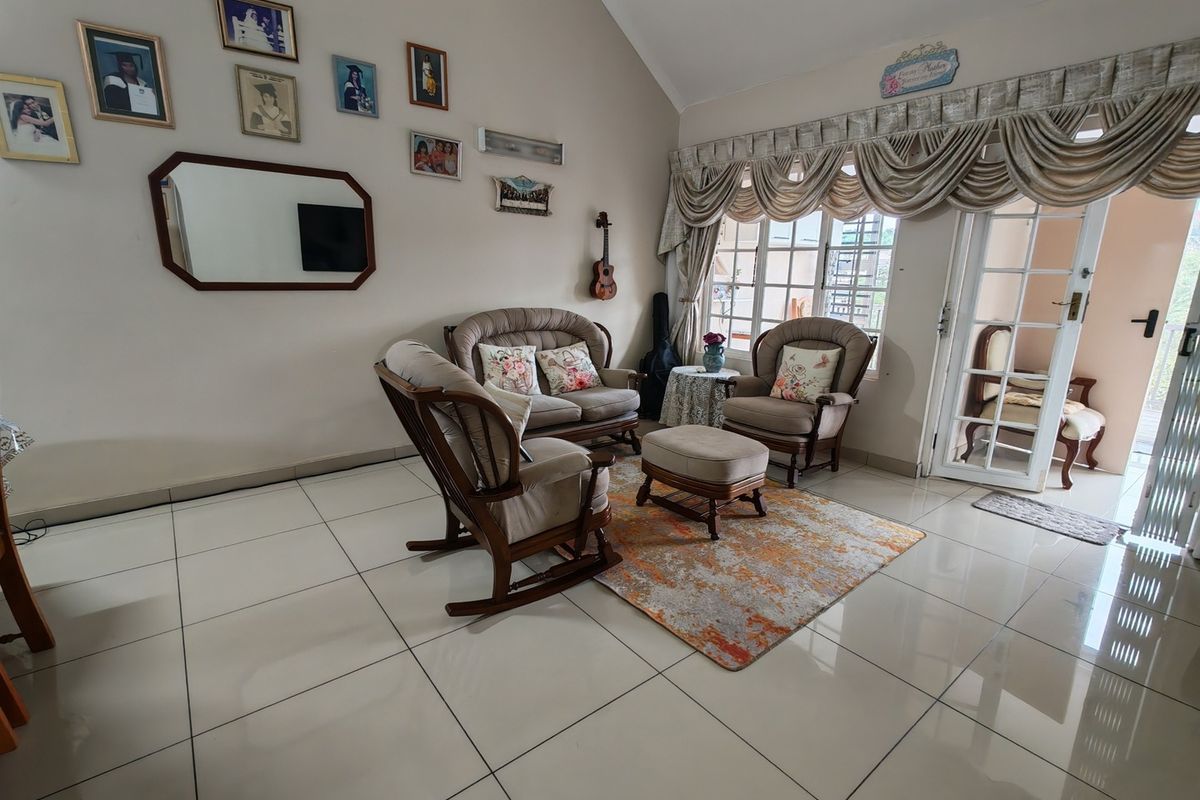Spacious living room featuring vaulted ceilings, large windows with security bars, tiled flooring, and direct access to an outdoor patio area.
