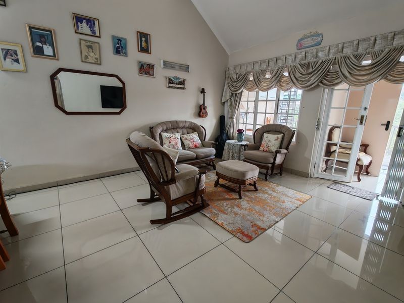 Spacious living room featuring vaulted ceilings, large windows with security bars, tiled flooring, and direct access to an outdoor patio area.