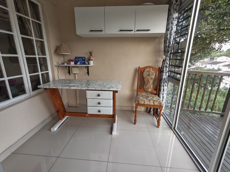 A bright home office space featuring tiled flooring, wall-mounted storage cabinetry, and large windows providing natural light and access to an outdoor balcony.