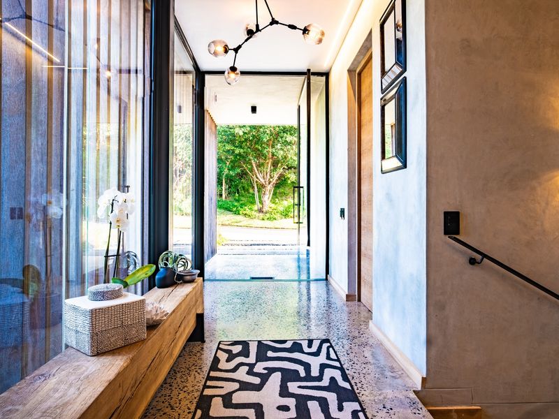 Modern entrance hall featuring polished terrazzo flooring, floor-to-ceiling glass panels, and a sleek metal handrail, leading to a bright outdoor garden view.