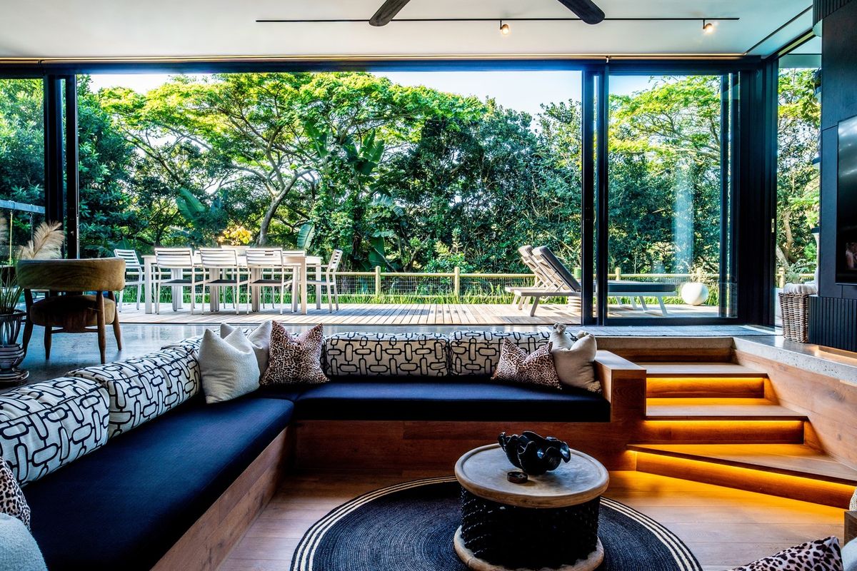 Modern sunken living room featuring built-in timber seating, integrated stair lighting, and expansive sliding glass doors opening onto a wooden deck.