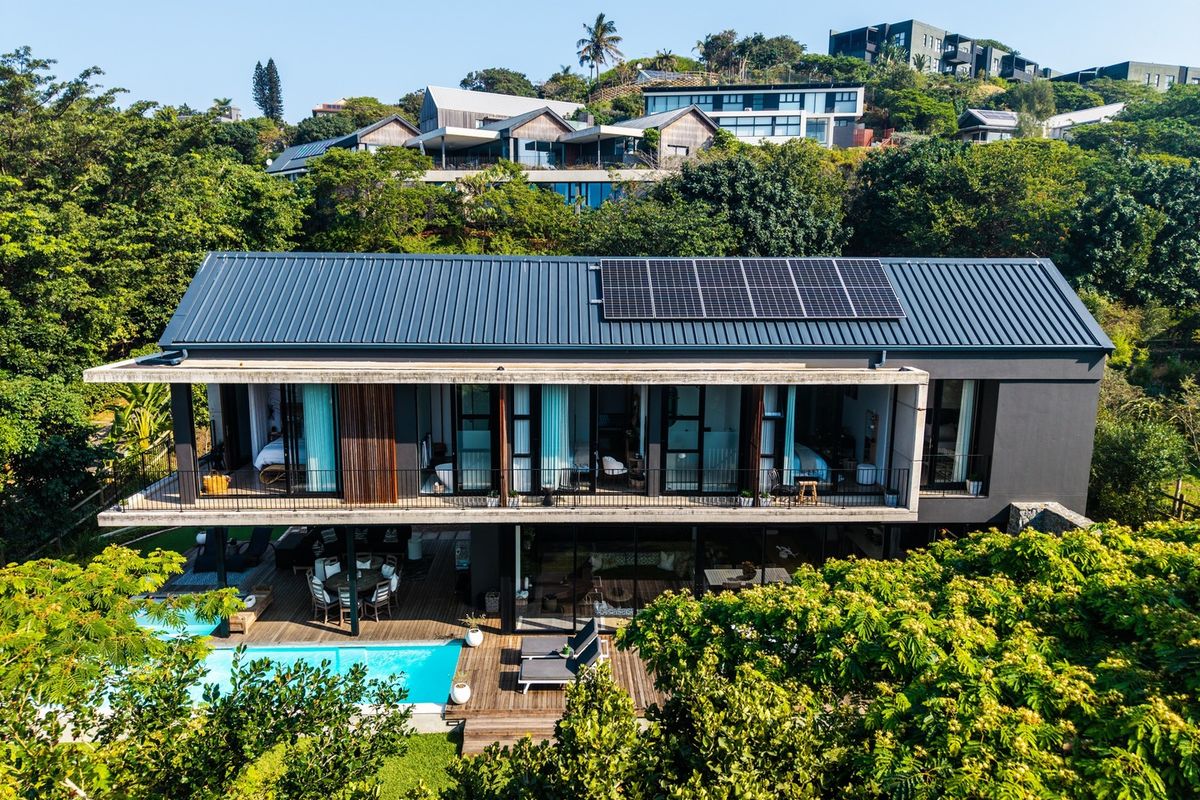 Aerial view of a modern multi-level home featuring a metal roof with solar panels, a swimming pool, and expansive timber decking.