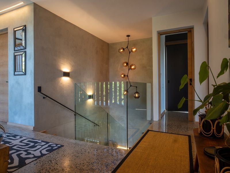 Modern hallway featuring polished concrete floors, a glass balustrade staircase, and contemporary feature lighting, creating a sophisticated and well-lit transition space.