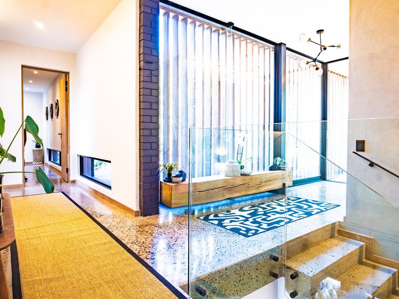 Modern entrance foyer featuring polished terrazzo flooring, a striking timber slat screen, and a contemporary concrete staircase with a glass balustrade.